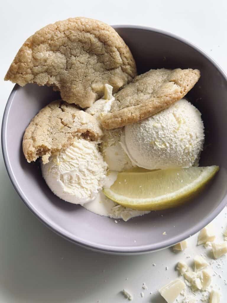 Two scoops of homemade vanilla ice cream served in a bowl with cookies and a lemon wedge