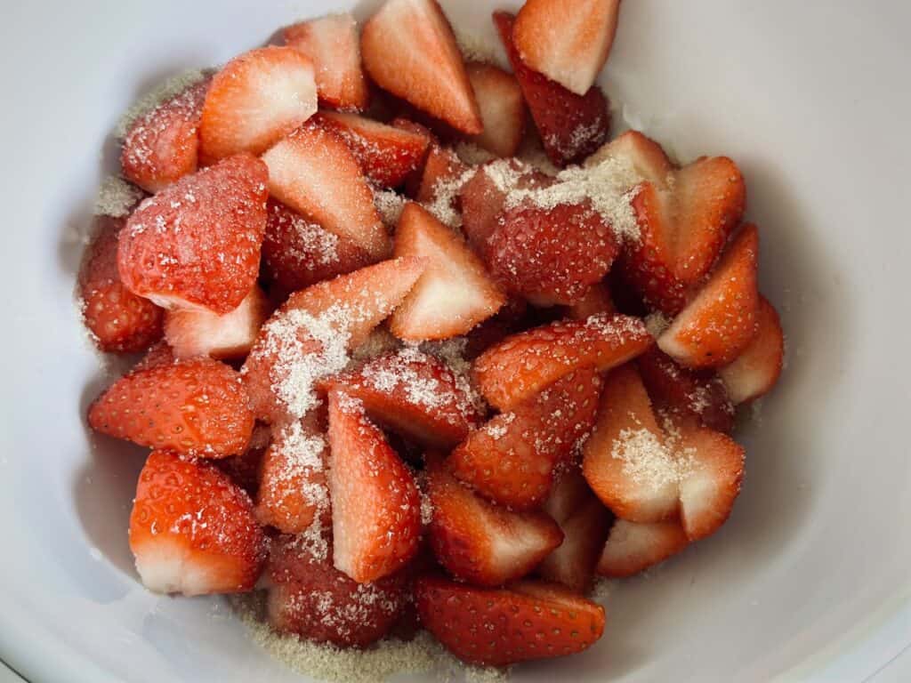 Slices of fresh strawberries in a bowl, mixed with granulated sugar and lemon juice, for the strawberry and mascarpone tartlets