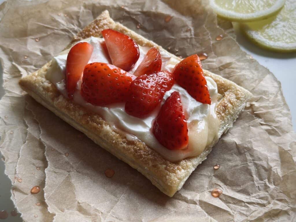 A strawberry and mascarpone tartlet with lemon curd, laid on parchment paper.