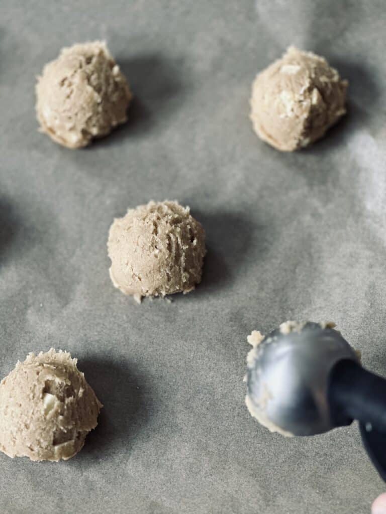Cookie dough balls laid on parchment paper and a baking tray.