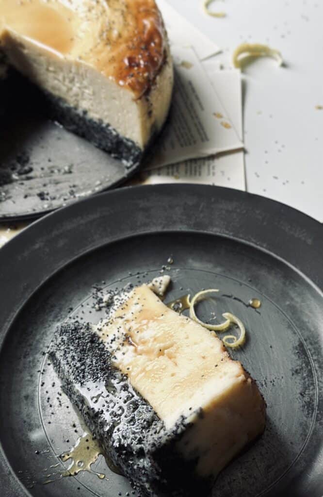 A slice of crustless poppy seed cheesecake decorated with honey glaze and lemon peel.
