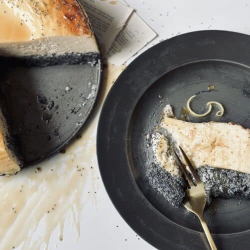 A plate with a slice of crustless poppy seed cheesecake with a golden fork slicing it.