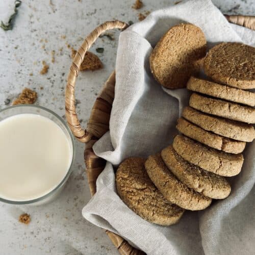 An arrangement of almond and rye cookies in a basket, next to a cup of milk