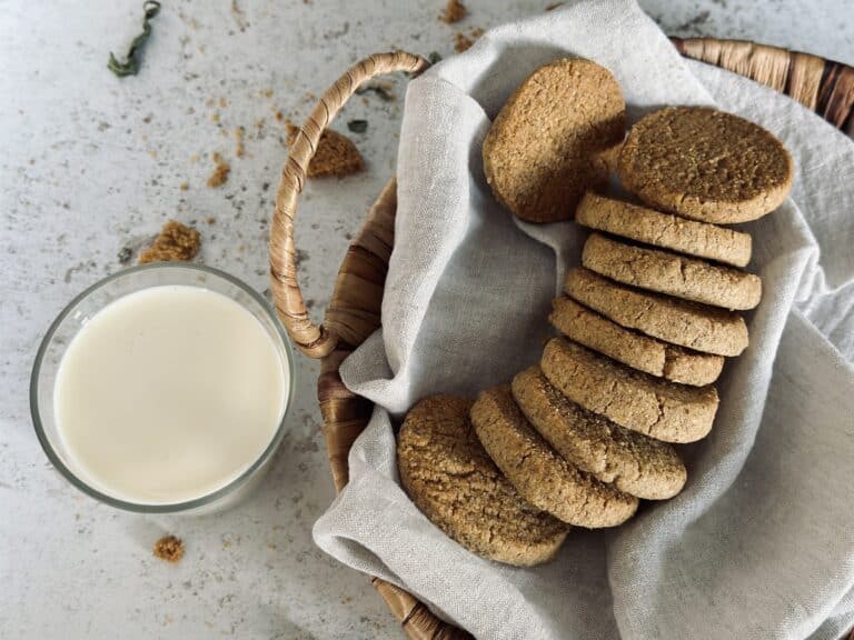 An arrangement of almond and rye cookies in a basket, next to a cup of milk