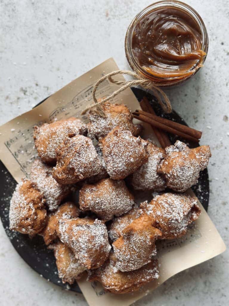 Fried donut bites on a plate with a jar of burnt caramel sauce next to it.