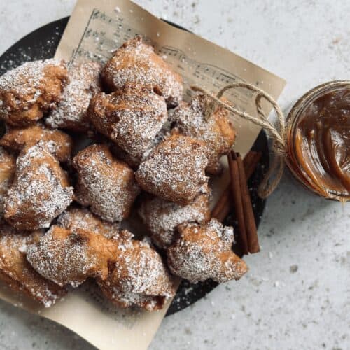 A plate full of fried donut bites next to a jar of burnt caramel sauce