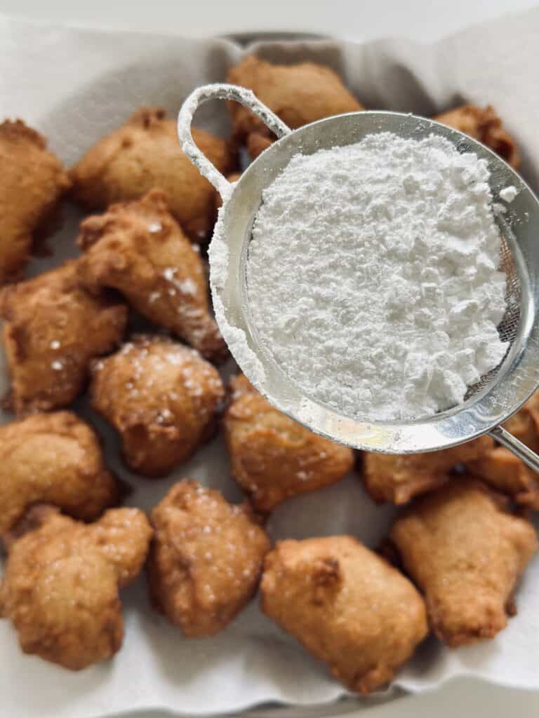 Dusting fried donuts with icing sugar.