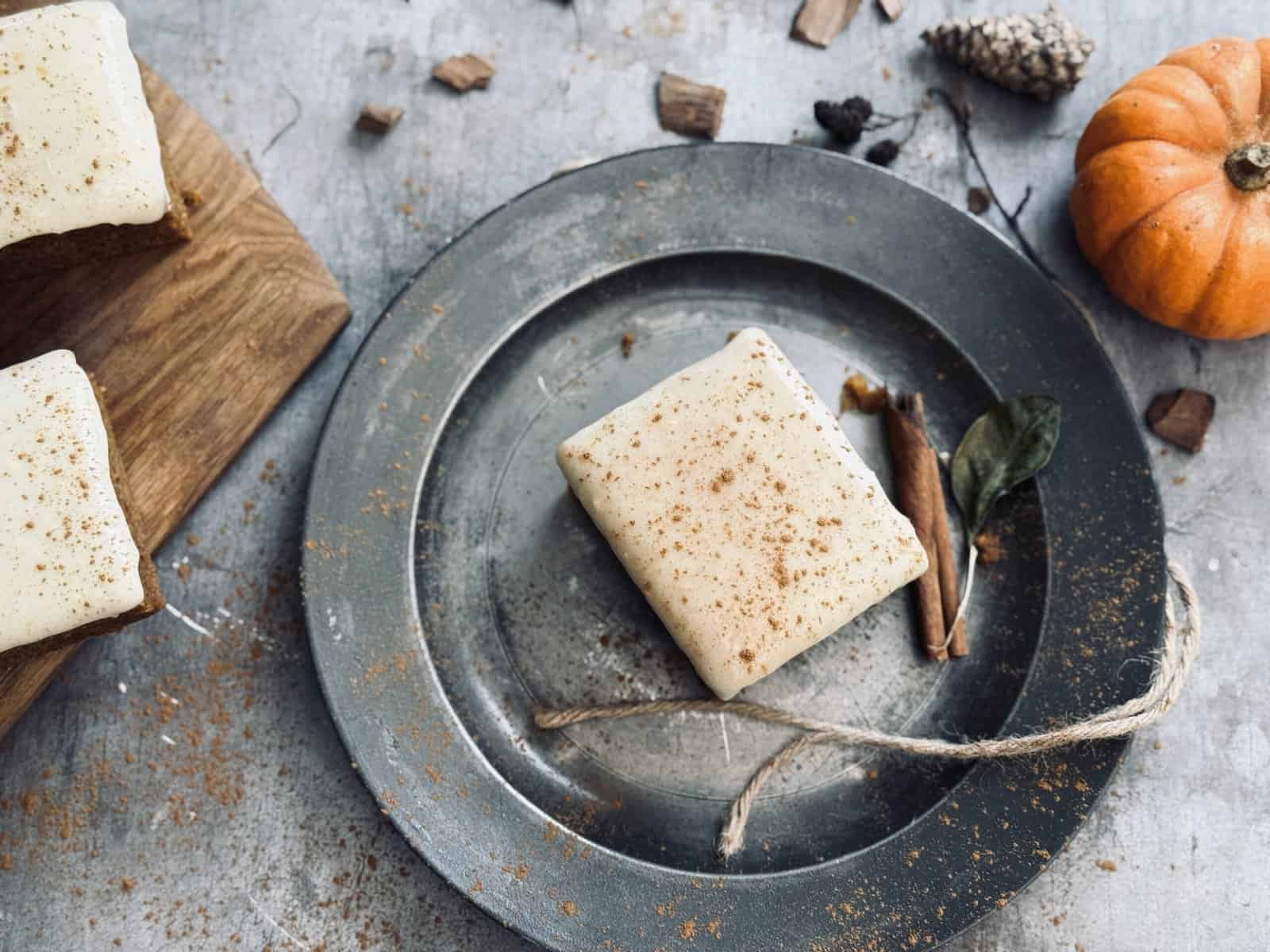 Sourdough pumpkin cake with cream cheese frosting on a metal plate decorated with cinnamon sticks and pumpkins.