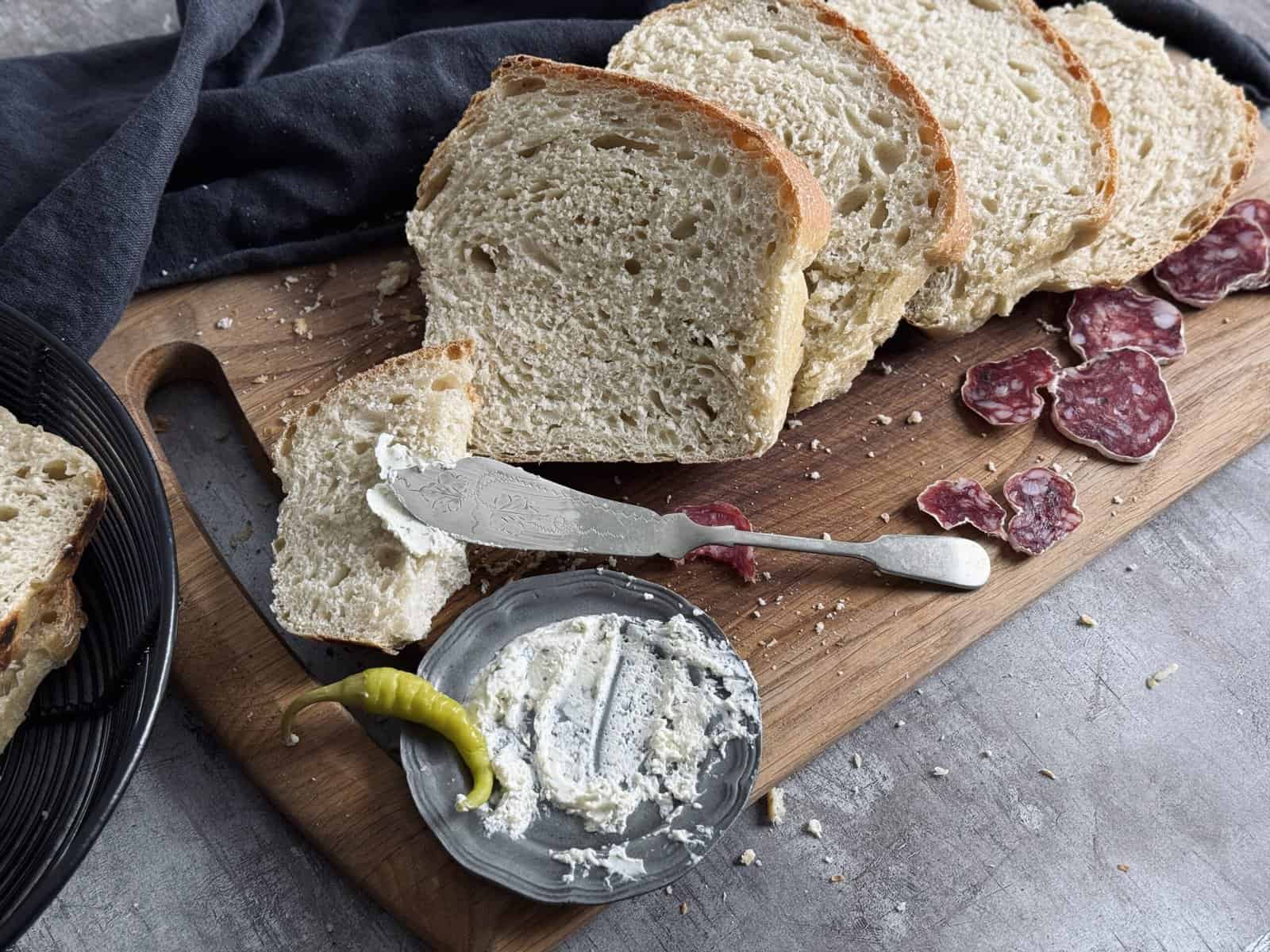A wooden cutting board with slices of bread and salami.