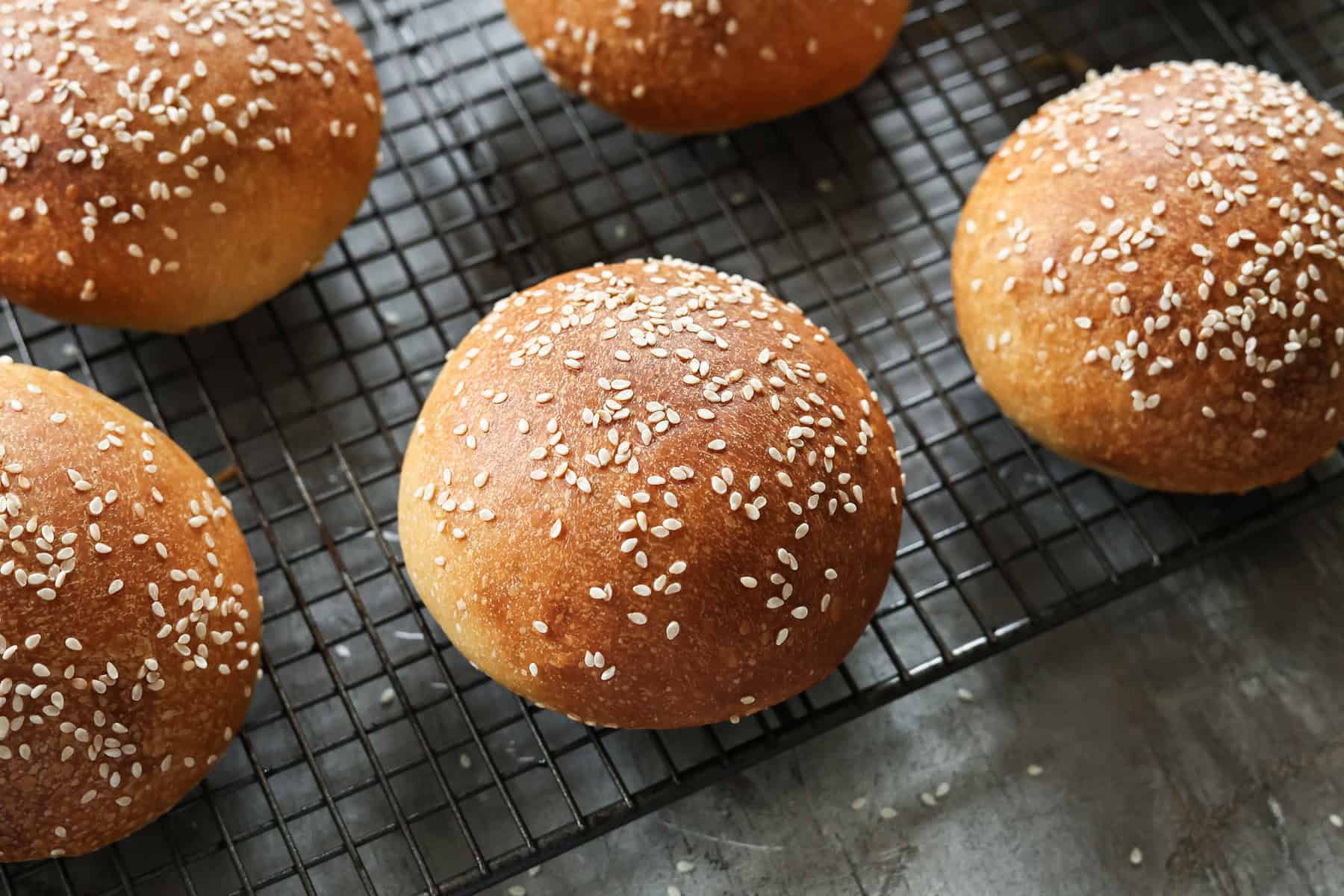 Some sourdough brioche burger buns on a wire rack.