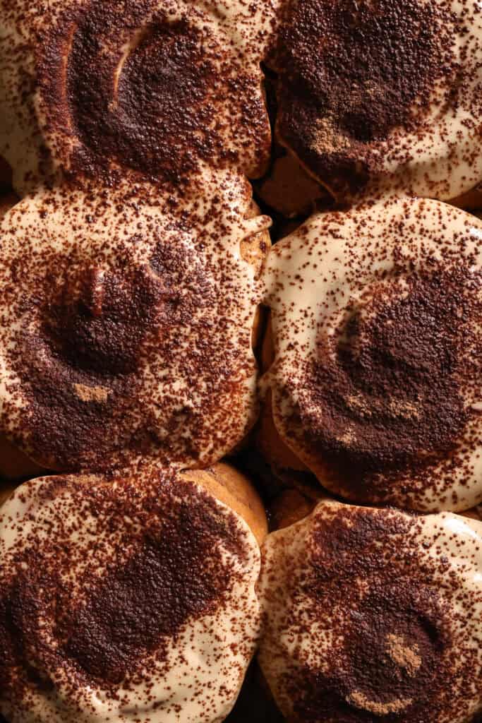 Close-up of 6 tiramisu cinnamon rolls with creamy espresso frosting and dusted with cacao powder.