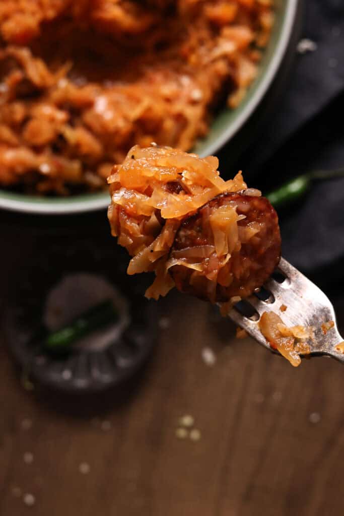 A fork with cooked sausage and cabbage 