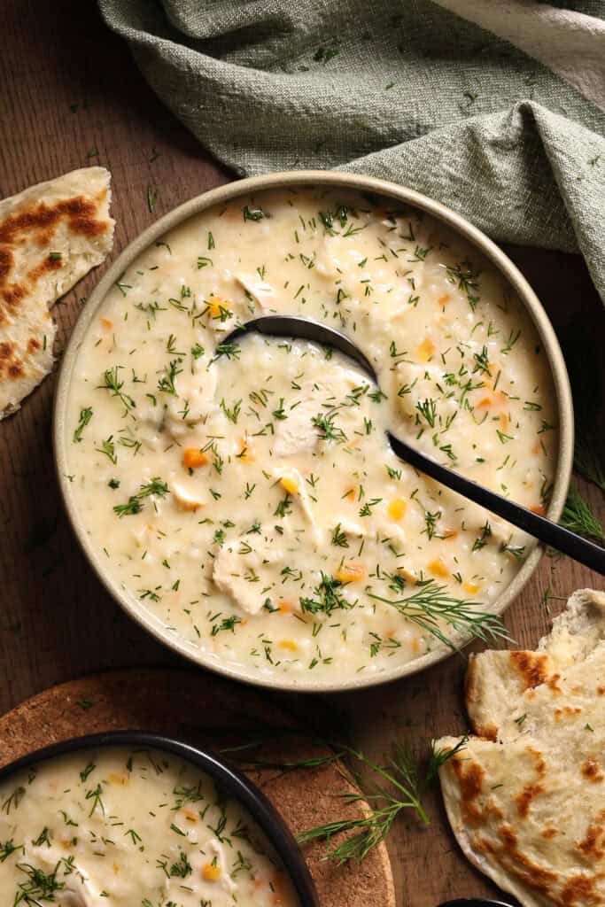A bowl of creamy chicken soup with rice and dill.
