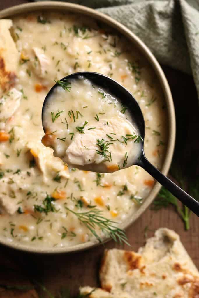 Close-up of a spoon full of creamy chicken soup with fresh dill.