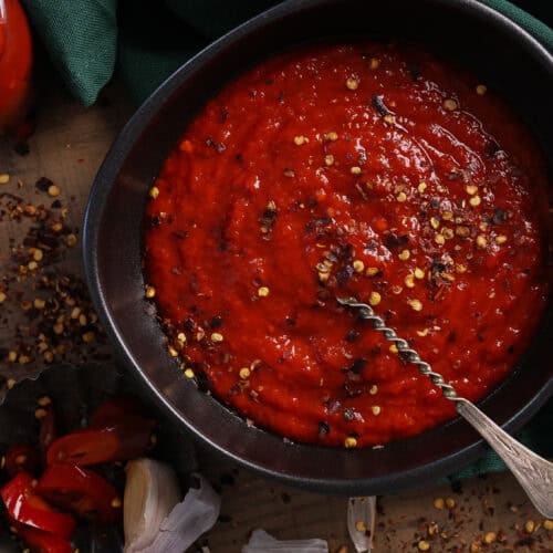 A black bowl with homemade hot sauce topped with crushed cilli flakes.