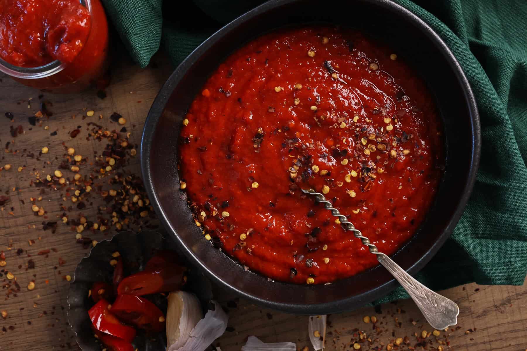 A black bowl with homemade hot sauce topped with crushed cilli flakes.