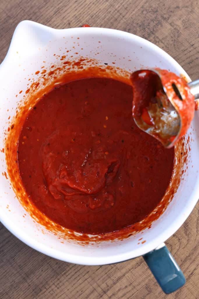 Mixing a hot sauce with an immersion blender in a bowl.
