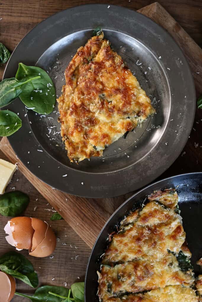 A slice of baked egg flatbread topped with cheese, mushrooms, and spinach.