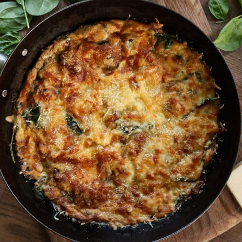 An iron skilled with a crispy baked egg flatbread topped with cheese, mushrooms, and spinach.
