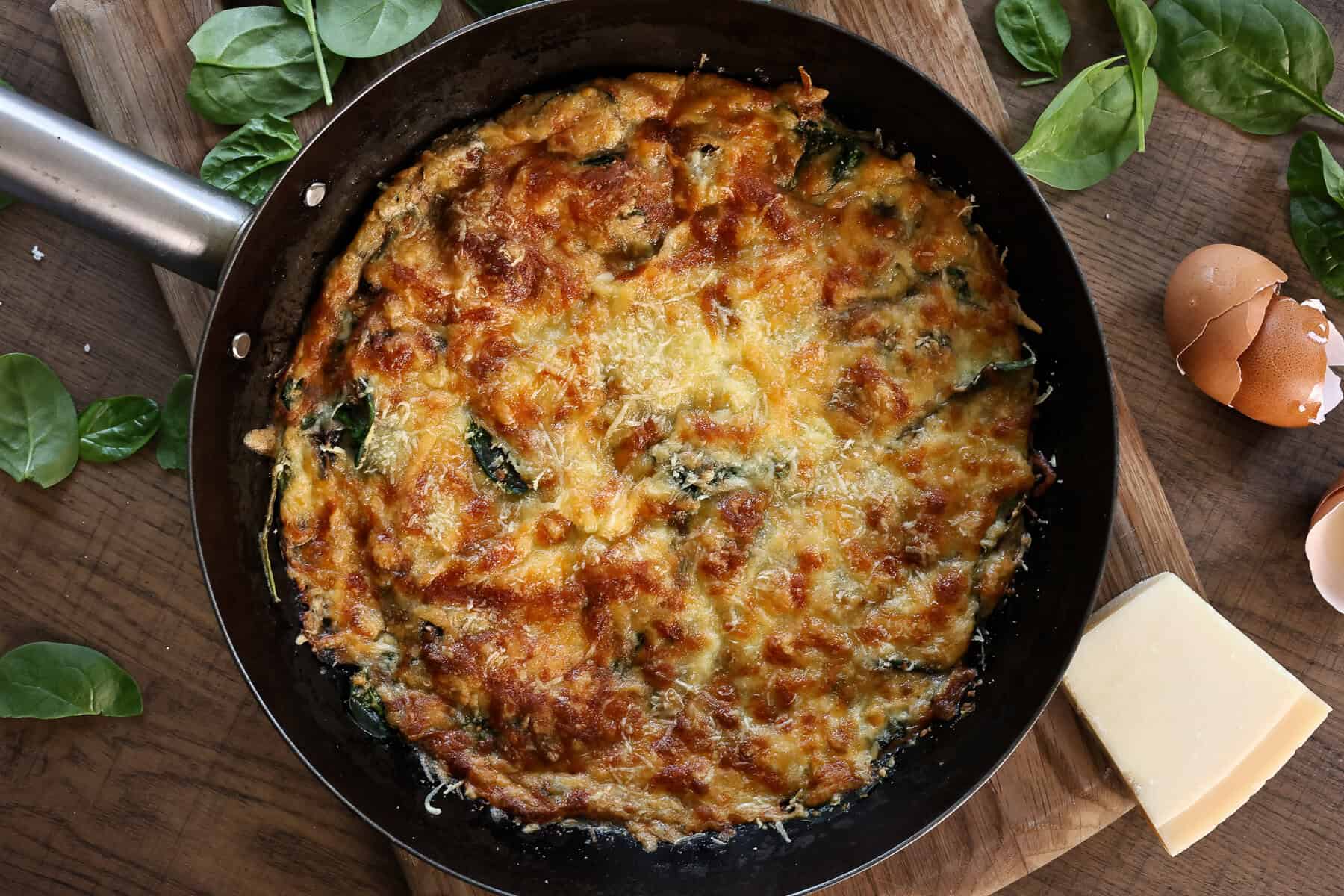An iron skilled with a crispy baked egg flatbread topped with cheese, mushrooms, and spinach.